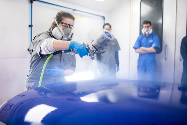 An auto collision repair student fixing a car's paint with a spray-painting tool